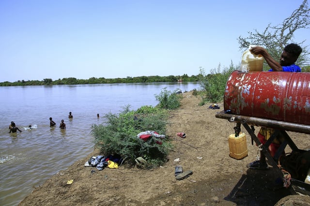 People swim in the Nile River as another fills a water container due to water outages in Khartoum, Sudan, Sunday, May 25, 2025. (AP Photo)