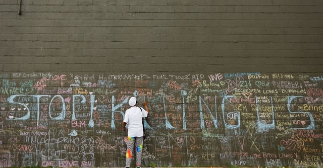 Woman leaves message in chalk at a memorial at the scene of a weekend shooting at a Tops supermarket in Buffalo, New York, U.S. May 20, 2022.  REUTERS/Lindsay DeDario