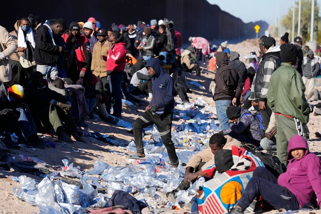 Hundreds of migrants, mostly from African countries, gather along the border, waiting to be brought into custody after breaking through gaps in the border wall on Dec. 5, 2023, in Lukeville, Ariz. (AP Photo/Ross D. Franklin)