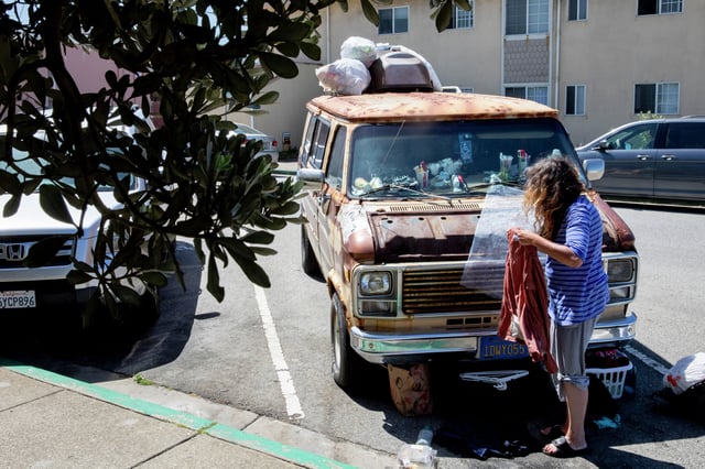 A woman washes clothes on the sidewalk near the van she resides in parked at the beachside intersection of Paloma Avenue and Beach Boulevard in Pacifica, Calif. 