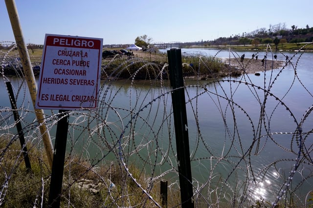 Migrants cross the Rio Grande into the U.S. from Mexico behind Concertina wire and a sign warning that it’s dangerous and illegal to cross, Wednesday, Jan. 3, 2024, in Eagle Pass, Texas. According to U.S. officials, a Mexican enforcement surge has contributed to a sharp drop in illegal entries to the U.S. in recent weeks. (AP Photo/Eric Gay)
