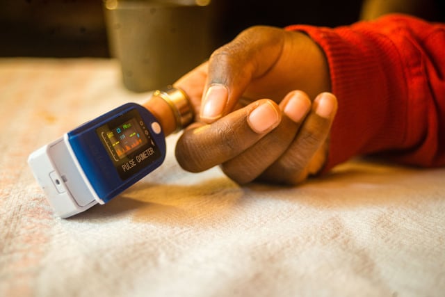 A closeup shot of a pulse oximeter on a black woman's finger to measure pulse rate and oxygen levels