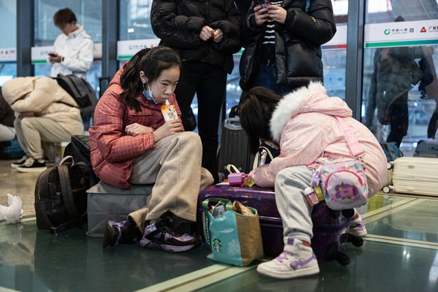 People sit with their luggage at Wuhan Railway Station after some trains were suspended due to freezing rain and snow in central China's Hubei province on Feb. 4, 2024.