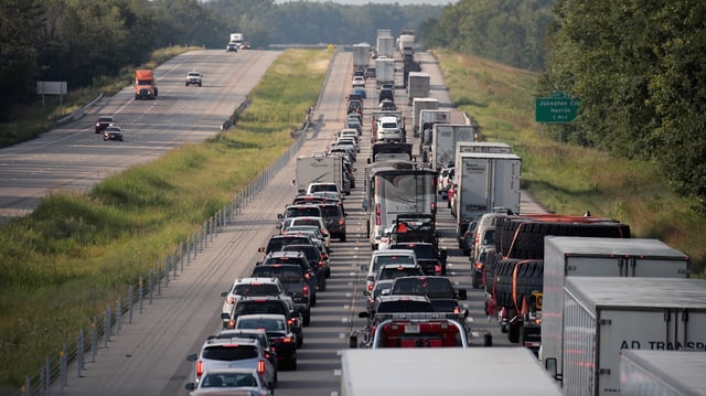 a photograph of three lanes of traffic completely backed up on the interstate. The lanes one the other side going in the opposite direction are mostly clear.