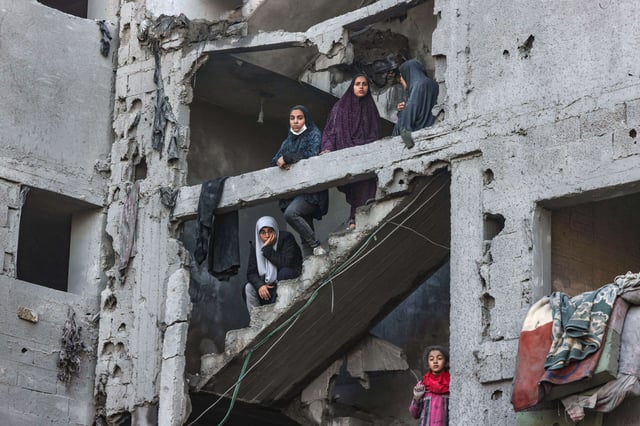 Palestinian women and children look on as they stand at the structure of a heavily damaged building on February 22, 2024, following overnight Israeli air strikes in Rafah refugee camp in the southern Gaza Strip.