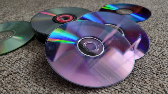 A collection of upturned CDs, DVDs and Blu-rays on a carpeted floor