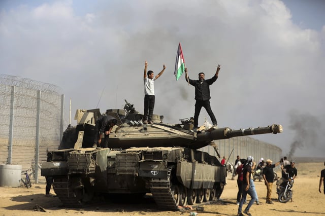 Palestinians wave their national flag and celebrate by a destroyed Israeli tank at the southern Gaza Strip fence east of Khan Younis Saturday, Oct. 7, 2023.