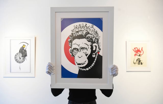 Gallery assistant Sophia Shim holds a limited edition print of Monkey Queen (2003) by Banksy, next to limited edition prints of Grin Reaper (2005, left) and Gangsta Rat (Red) (2004, right), part of the 'Catch Me If You Can' exhibition, at the HOFA Gallery in Mayfair, London. (Photo by Kirsty O'Connor/PA Images via Getty Images)