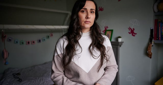 Sarah, one of the four Mums in the story, on set in a child's bedroom, wider shot...The actor playing Sarah is Sarah Barlondo. She is wearing a jumper and is looking solemnly ahead.