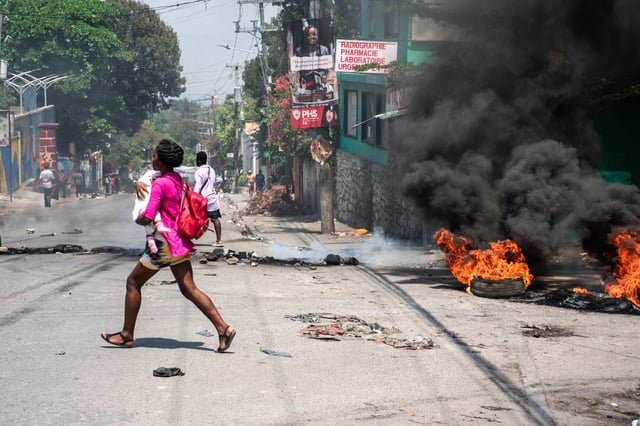 A woman carrying a child runs from the area after gunshots were heard in Port-au-Prince, Haiti, on March 20, 2024.