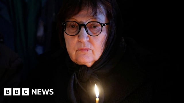 Lyudmila Navalnaya holds a candle, looking sad