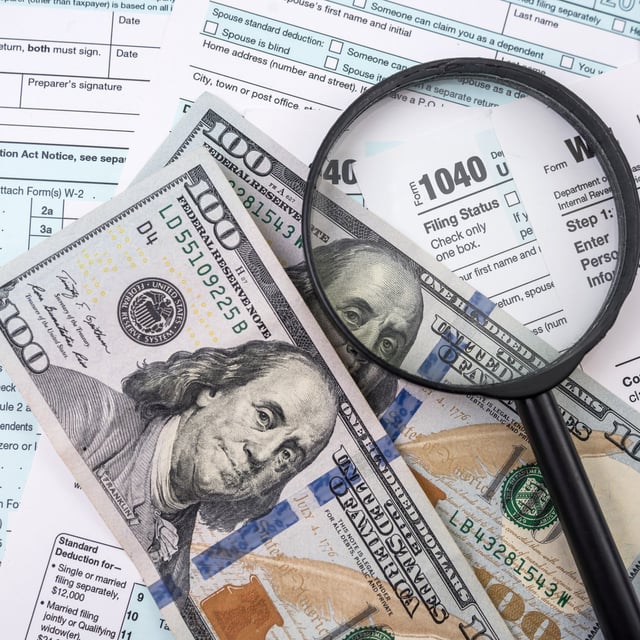 A stock image of U.S. tax forms and dollars with a magnifying glass. The IRS has said time is running out to claim refunds for the 2020 tax year.