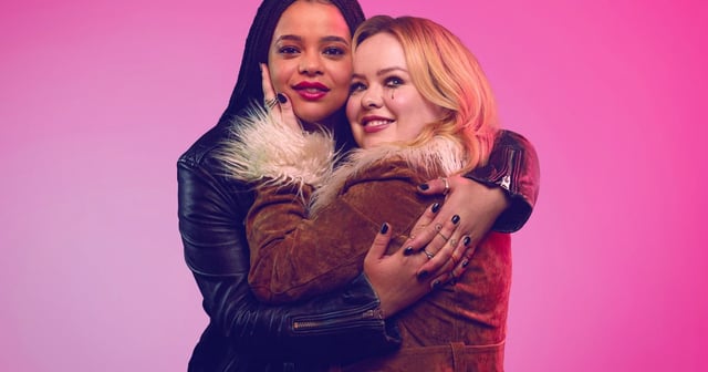 Eddie and Maggie hugging in front of a pink backdrop, with an RT four star banner in the bottom right corner