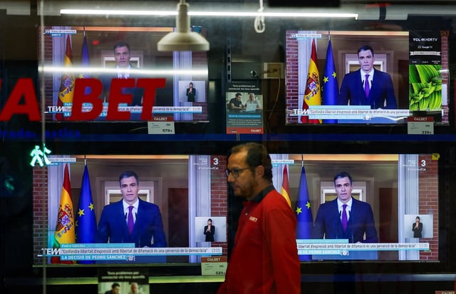 A person walks next to TVs broadcasting the statement by Spain’s Prime Minister Pedro Sanchez on Monday. Photo: Reuters