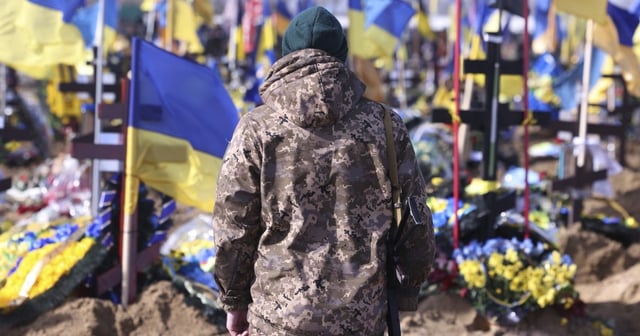 A Ukrainian soldier stands in front of the graves of Ukrainian soldiers killed in the war at a cemetery in Kharkiv.