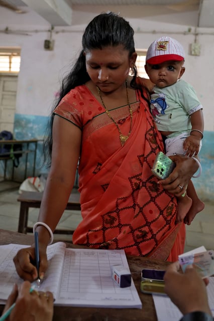 A woman holds her son as prepares to cast her vote at a polling station after the end of the third phase of India's general election, in Valia village in Bharuch district in the western state of Gujarat, India, May 7, 2024.