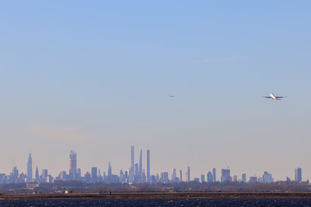 A passenger aircraft takes off from JFK international Airport in New York as the Manhattan skyline looms in the distance on February 5, 2024.
