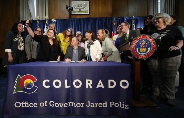FILE - Colorado State Sen. Julie Gonzales, third from left, takes a photo of state Rep. Brianna Titone, Colorado Gov. Jared Polis, state Sen. Sonya Jaquez Lewis and state Rep. Meg Froelich and others before Polis signed the first of three bills that enshrine protections for abortion and gender-affirming care procedures and medications, April 14, 2023, in the State Capitol in Denver. Voters in both Colorado and South Dakota will have a say on abortion rights this fall after supporters collected enough valid signatures to put measures on the ballot.