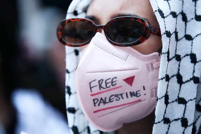 A protester with a medical mask reading "FREE PALESTINE" participates in an outdoor protest