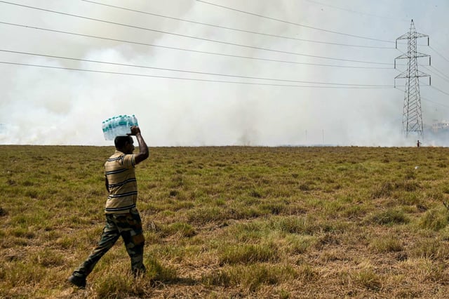 A man carries water bottles while forest personnel douse a fire as smoke billows at a marshland in a suburb of Chennai. India is enduring a crushing heatwave, with temperatures in several cities above 45 degrees Celsius. Photo: AFP