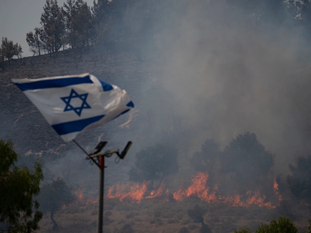 An Israeli flag flutters next to a fire burning in an area near the border with Lebanon, northern Israel in Safed, Wednesday, June 12, 2024. Scores of rockets were fired from Lebanon toward northern Israel on Wednesday morning, hours after Israeli airstrikes killed four officials from the militant Hezbollah group including a senior military commander. (AP Photo/Leo Correa)