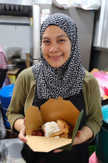 Aidah Rahim, Hassan’s wife, holds a box of “nasi lemak”, a popular rice dish that is their stall’s speciality. Photo: AP