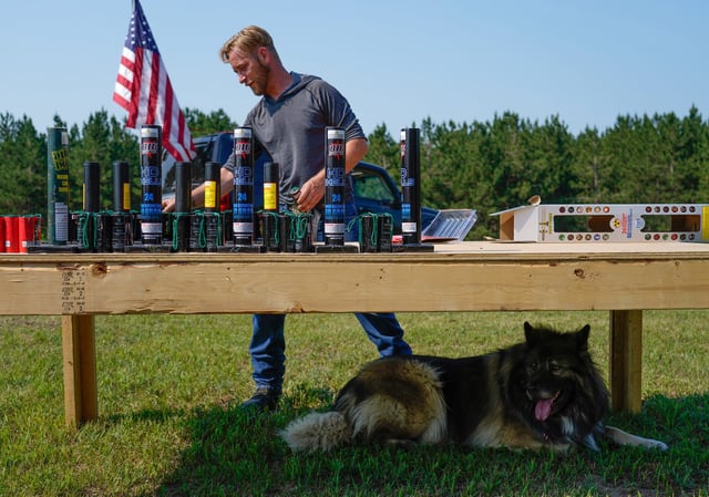 Josiah Sharrett (center) of Newberry unpacks firework mortars as his dog Samba rests beneath the launch pad before his fireworks show at Schubach Farms in Newberry on Saturday, July 3, 2021.
