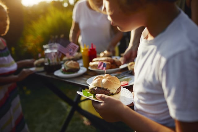 Multi generations on picnic in back yard eating burgers and celebrating 4th of July - Independence Day.