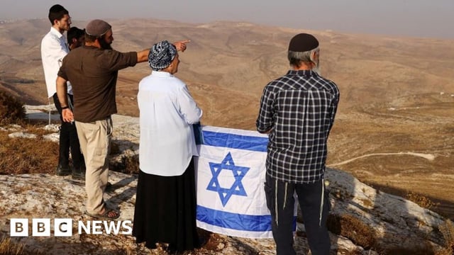 A group of Israelis with an Israeli flag look out across hilltops in the occupied West Bank (November 2022)