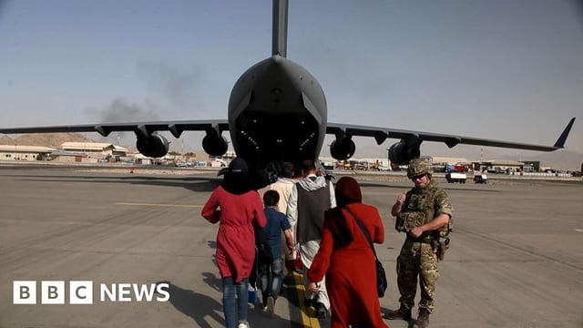 A member of British armed forces alongside Afghans boarding a plane at Kabul Airport in August 2021
