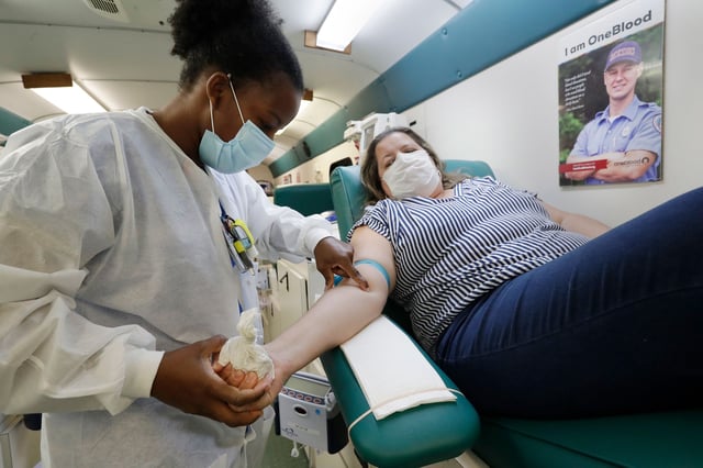 Phlebotomist Josianne Fiefie, left, looks for a vein as Maria Teresa Andreychuk prepares to donate blood aboard a OneBlood blood donation bus, Wednesday, April 22, 2020, in Miami.