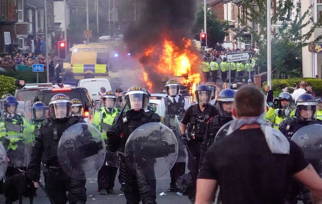 Riot police hold back protesters near a burning police vehicle on July 30, 2024 in Southport, England. CREDIT: Getty Images