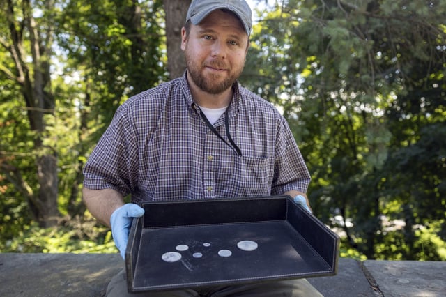 This photo, provided by the U.S. Military Academy at West Point, Aug. 30, 2023, shows West Point archeologist Paul Hudson displaying coins found in the lead box believed to have been placed in the base of a monument by cadets almost two centuries ago, in West Point, NY. The nearly 200-year-old West Point time capsule, that appeared to yield little more than dust when it was opened during a disappointing livestream earlier this week, contained hidden treasure after all, the U.S. Military Academy said Wednesday.