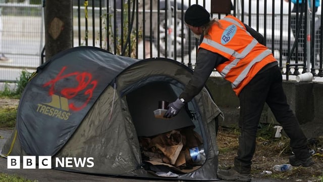 A worker in a high viz orange vest clearing rubbing from a green tent in Dublin