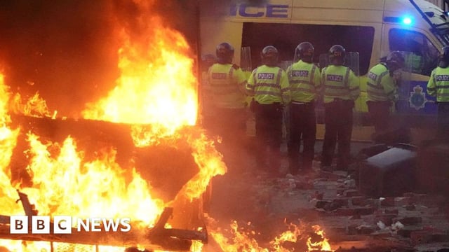 Riot police hold back protesters near a burning police vehicle after disorder broke out on in Southport