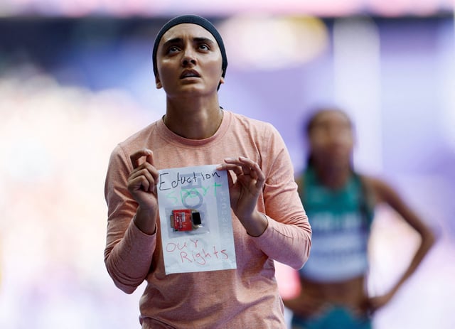 Kimia Yousofi of Afghanistan holds up a sign that reads "Education, Sport, our right" in the colors of the Afghanistan flag after competing at the Paris 2024 Olympics Women's 100m Preliminary Round in Saint-Denis, France on August 2, 2024.