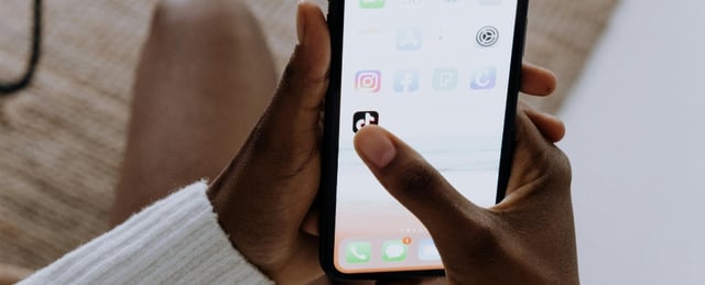Hands holding a phone about to click on the TikTok app