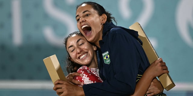 Silver medallists Canada's Melissa Humana-Paredes (L) celebrates with gold medallists Brazil's Eduarda Santos Lisboa on the podium for the victory ceremony of the women's beach volleyball event during the Paris 2024 Olympic Games at the Eiffel Tower Stadium in Paris on August 9, 2024.