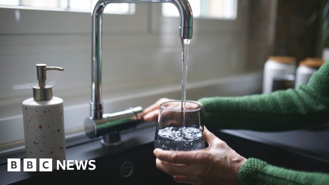 A person turning on a tap to fill a glass of water