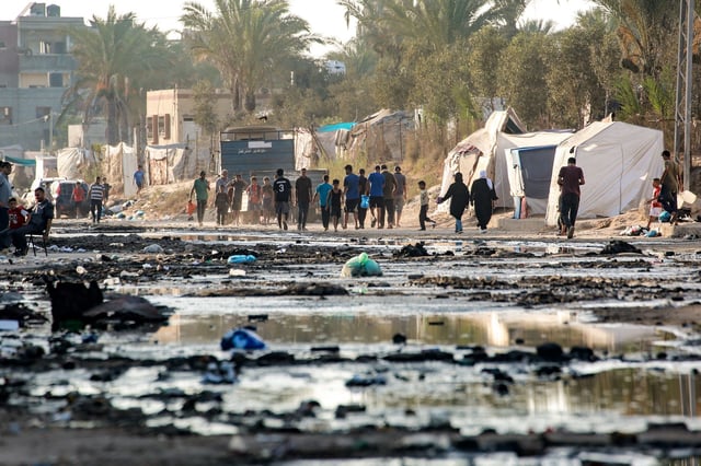 Palestinians walk near tents used as shelter along a street covered with stagnant wastewater in Deir el-Balah, in the central Gaza Strip on July 19, 2024.