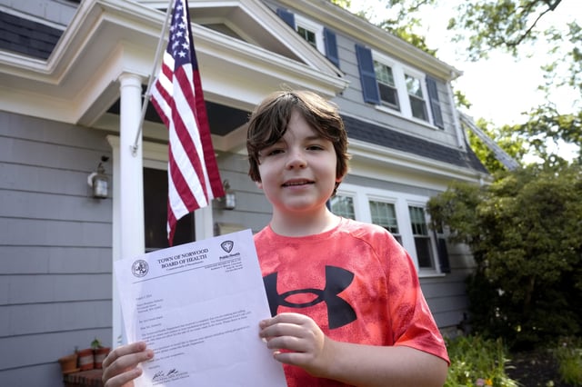 Danny Doherty, 12, of Norwood, Massachusetts, stands for a photograph Wednesday, August 21, 2024, in front of his home in Norwood, while holding a letter from the Town of Norwood Board of Health advising his family that they may not sell homemade ice cream at an ice cream stand near their home. (Steven Senne / AP)