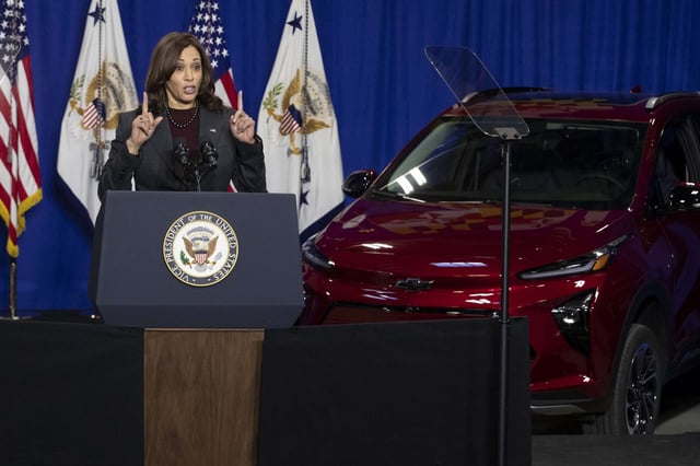 Vice President Kamala Harris gives a speech in front of a red electric vehicle.