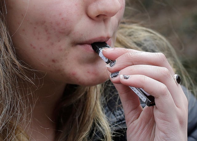 FILE - In this April 11, 2018, file photo, a high school student uses a vaping device near a school campus in Cambridge, Mass. With the Food and Drug Administration recently calling e-cigarettes an epidemic among teenagers, Arizona is stepping up efforts to keep youths from vaping. Arizona health officials are launching an anti-vape campaign in December and pursuing e-cigarette businesses aimed at minors. (AP Photo/Steven Senne, File)