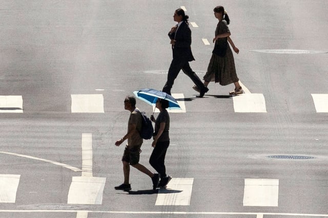 A pedestrian crosses a street holding an umbrella to protect herself from the sun during a heatwave, in downtown Los Angeles, on Sept. 6, 2024.