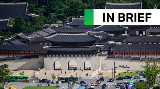 People walk past Gyeongbokgung Palace as people drive their vehicles along a main road past a statue of King Sejong at Gwanghwamun Square in Seoul.
