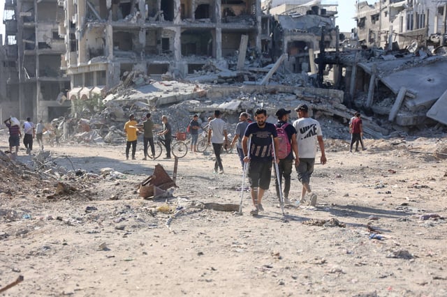 A Palestinian man on crutches walks on the dirt of a destroyed road past collapsed buildings after the Israeli military withdrew following a two-week offensive from the Shujaiya neighbourhood, east of Gaza City, on July 10, 2024.