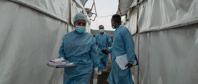 Health workers walk between wards at the Mpox treatment centre at Nyiragongo General Referral Hospital, north of Goma on August 17, 2024. With around 16,000 cases recorded since the beginning of the year, the DRC is the focus and epicentre of the epidemic that led the World Health Organisation (WHO) to trigger its highest level of alert at the international level on Wednesday. The province of South Kivu records around 350 new cases per week, according to Dr Justin Bengehya, epidemiologist at the provincial health division of South Kivu. Goma, capital of the province of North Kivu, almost surrounded by an armed rebellion and where hundreds of thousands of displaced people are crammed into makeshift camps, fears a large-scale spread due to promiscuity. (Photo by GUERCHOM NDEBO / AFP)