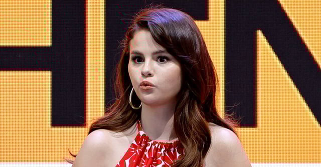 Selena Gomez at an event, wearing dangling earrings and headphones